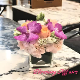 Pink and purple flowers arranged in a square glass vase