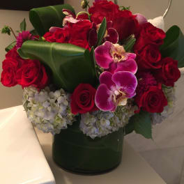 Red roses and purple orchids in a dark green vase