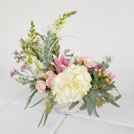 Basket arrangement with pink roses, white hydrangea, and tall white blooms