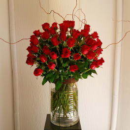 A tall bouquet of red roses in a clear glass vase