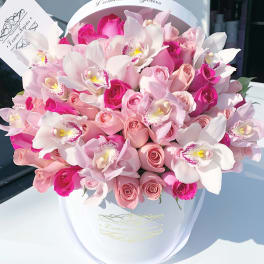 Hatbox arrangement of pink roses and white orchids in a white round box with a card.