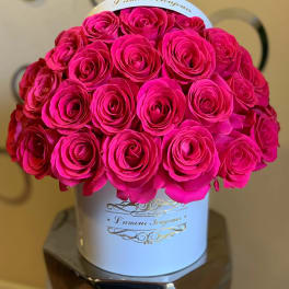 Round bouquet of bright pink roses arranged tightly in a white hatbox-style container.