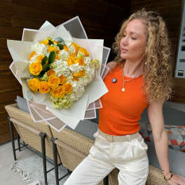 Large bouquet of yellow roses and white hydrangeas wrapped in white paper, held by a person.