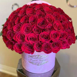 Large dome of red roses arranged in a pink round hat box with gold script on the front