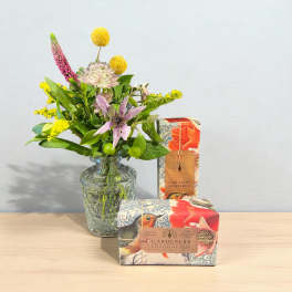 Small mixed flower bouquet in a glass vase beside two boxed soaps