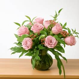 Pink roses arranged in a green glass vase with leafy greenery