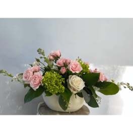 Pink and white roses in a white bowl vase with green accents