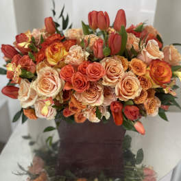 Bouquet of peach and orange roses with red tulips in a dark vase