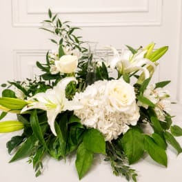 White floral arrangement with lilies, roses, and a clear glass cross