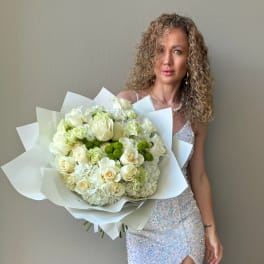 Large white and green bouquet of roses and hydrangeas wrapped in paper, held by a woman in a sequin dress