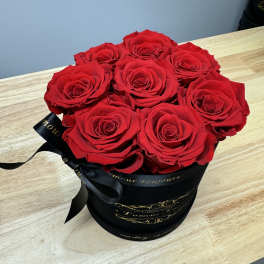 Round black hat box filled with tightly packed red roses on a light wood table