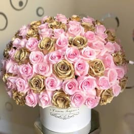 Dome of pink and gold roses arranged densely in a white hatbox-style container on a pedestal