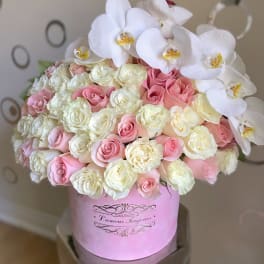 Round box arrangement of white orchids and pink and cream roses in a pink hatbox.