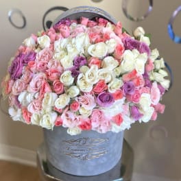 Large arrangement of pink, white, and lavender roses in a gray hatbox.