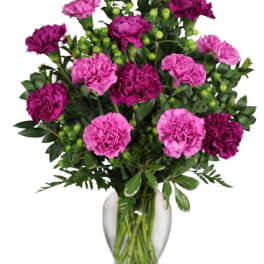 Vase of bright magenta and purple carnations with green berry accents in a clear glass vase