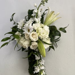 White lilies, roses, and daisies arranged on a moss-covered hanging cross.