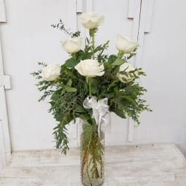 White roses arranged in a clear glass vase with a white ribbon