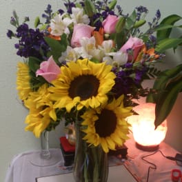 Bouquet of sunflowers, pink roses, and white lilies in a glass vase
