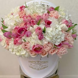 Pink and white tulips, roses, hydrangeas, and carnations in a white hatbox container.