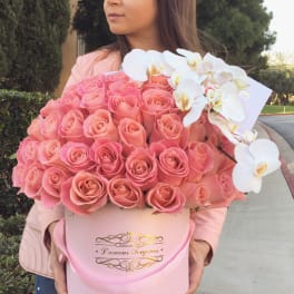 Large round pink hatbox of pink roses with white orchids, held by a person outdoors
