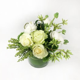 White roses arranged in a green glass vase with green accents