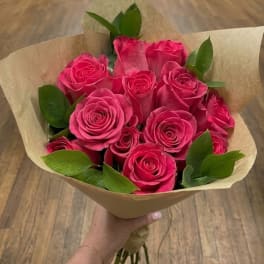 Handheld bouquet of bright pink roses wrapped in tan paper