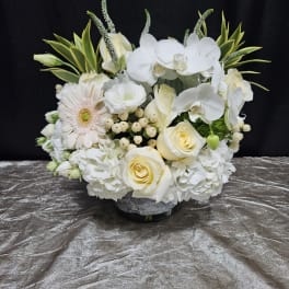 White floral arrangement with roses, orchids, and a gerbera daisy in a low vase