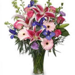 Mixed bouquet of pink lilies, gerbera daisies, and purple flowers in a glass vase