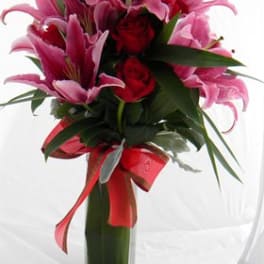 Pink lilies and red roses in a tall glass vase with a red ribbon