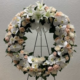 Large floral wreath with white orchids, lilies, and pale roses on a stand