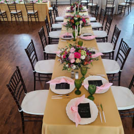Long banquet table with low mixed pink and white floral centerpieces, white tapers, and place settings.