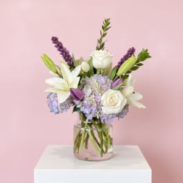 White lilies and roses with lavender hydrangeas in a glass vase