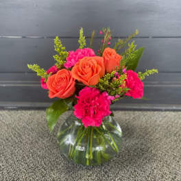 Orange roses and hot pink carnations in a clear glass vase