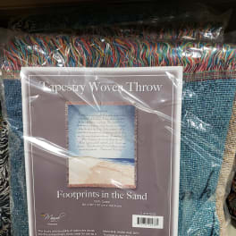 Packaged woven throw blanket with multicolored fringe and a beach scene label