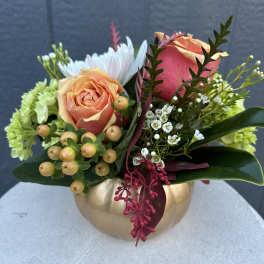 Peach and pink roses arranged in a gold pumpkin vase