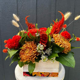 Red and orange floral arrangement in a wooden box with green leaves