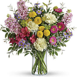Mixed bouquet of pink, yellow, purple, and white flowers in a glass vase