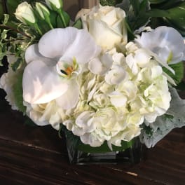 White roses, hydrangeas, and calla lilies arranged in a glass vase