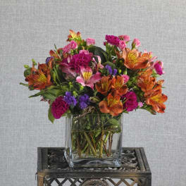 Colorful bouquet of orange, pink, and purple flowers in a clear glass vase