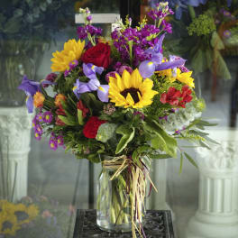 Mixed bouquet with sunflowers, roses, and purple iris in a glass vase