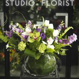 Purple and white floral arrangement in a round glass vase