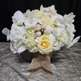 White floral bouquet with roses, orchids, and hydrangeas tied with burlap ribbon