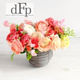 Pink and peach flower arrangement in a gray basket vase