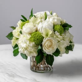 White roses and hydrangeas in a clear glass vase with green accents