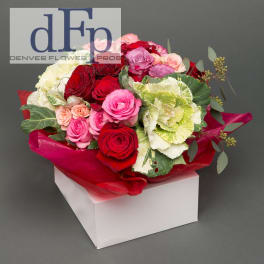 Bouquet of red, pink, and white roses with ornamental cabbage in red wrap