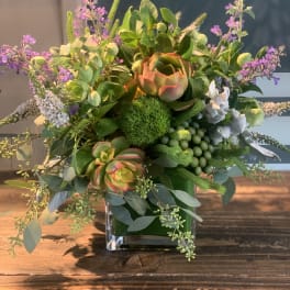 Mixed floral arrangement in a square glass vase with green succulents and purple accents