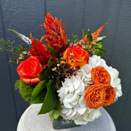 Orange roses and white hydrangeas in a glass vase with red plumes