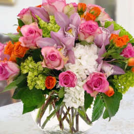 Mixed bouquet of pink roses, lavender orchids, and white hydrangea in a glass vase