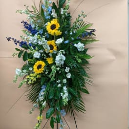 Standing floral spray with sunflowers, blue and white flowers, and greenery