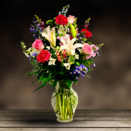 Mixed bouquet of lilies, roses, carnations, and purple daisies in a glass vase